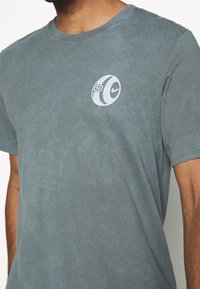 Camiseta de algodón gris con un logo circular de Nike y el número "10" en blanco en el pecho. Textura suave, mangas cortas, corte clásico.