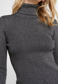 Grå räfflad polokrage med metalltråd. Har en figurnära design och mjuk textur, vilket framhäver vertikala ränder genom hela plagget.