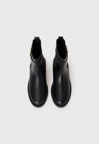Bottines en cuir noire avec une finition lisse, bout arrondi, semelle en caoutchouc plate et languettes de tirage. Présente des détails en métal doré sur le côté.