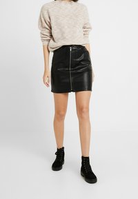 Black leather skirt with a front zipper, paired with a light knit sweater. The outfit includes black lace-up ankle boots.