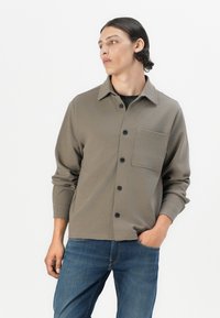 Grey long-sleeve shirt with a collar, front pocket, and black buttons, paired with blue jeans. Smooth texture with a casual fit.