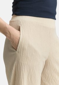 Pantalons texturés beige clair avec un motif côtelé vertical subtil et des poches latérales, associés à un haut côtelé bleu marine.