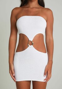 Robe bodycon tricotée blanche sans bretelles, avec une découpe en forme de clé à la taille et un connecteur accent en or.