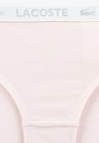 Light pink cotton underwear featuring a white waistband with gray "LACOSTE" logo, smooth texture, and classic brief design.