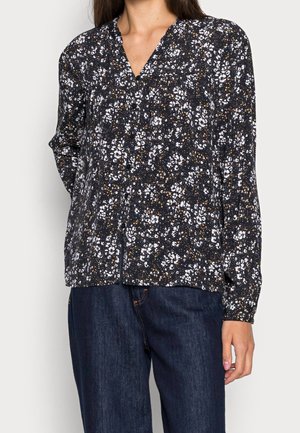 Langärmlige schwarze Bluse mit weißem Blumenmuster, V-Ausschnitt, lockere Passform und weichem Stoff. Kombiniert mit dunkelblauen Jeans.