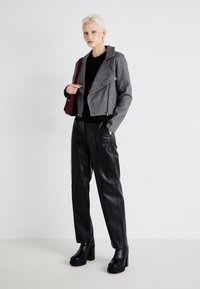 Gray cropped jacket with a broad collar, zip details, black top, glossy black leather trousers, and chunky heeled boots. Burgundy bag accent.