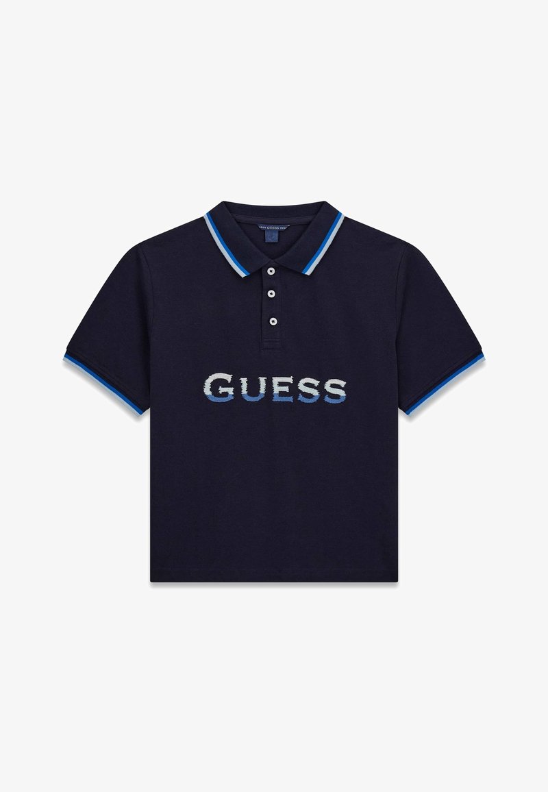 Polo bleu marine à manches courtes, avec une patte de boutonnage à trois boutons, un col et des poignets rayés bleu et blanc, et le logo "GUESS" en dégradé bleu sur la poitrine.