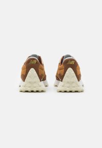 Braune textile Sneaker mit weißer Gummisohle, dreieckigem Absatz und erhabenen Punkten. Mit einem goldenen Logo auf der Rückseite und grauen Akzenten.