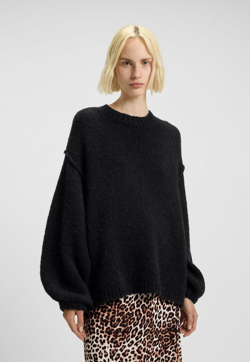 Maglione nero lavorato a maglia con una vestibilità comoda, colletto a coste e maniche voluminose, abbinato a una gonna a stampa animale decorata.
