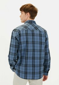 Blå- og sortternet skjorte med knaplukning, lange ærmer, krave og rundet kant. Lavet af blødt stof, med et standard fit og synlige syninger.