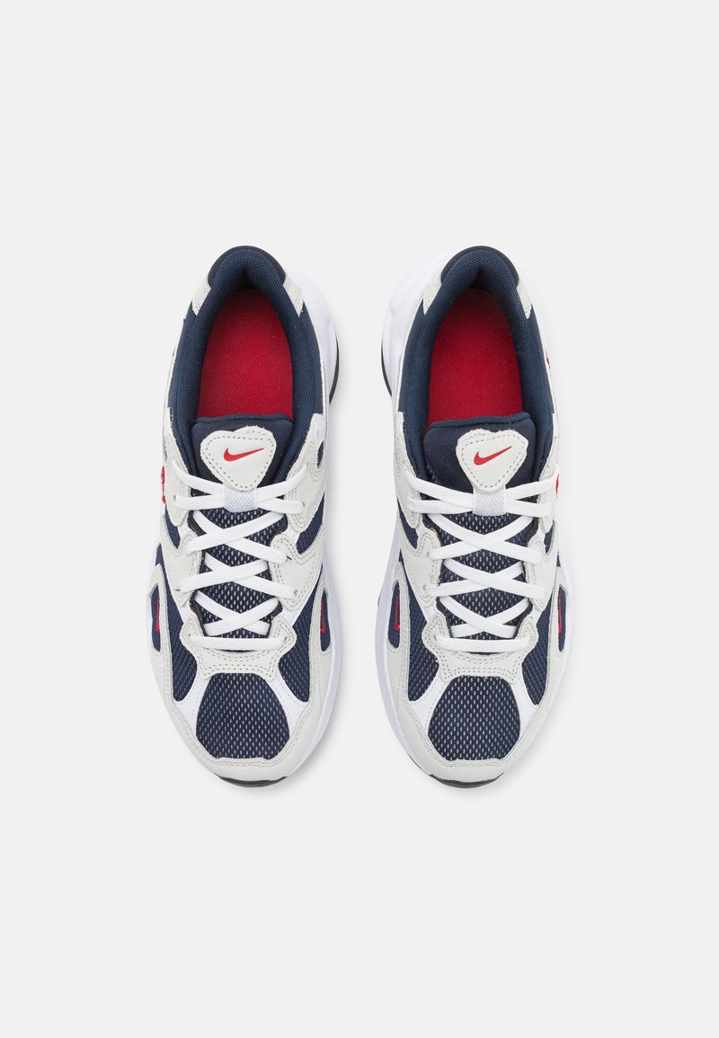 Zapatillas Nike con una parte superior de malla blanca, acentos en azul marino, detalles rojos en la lengua y una suela texturizada. Presenta cordones blancos y el logo.