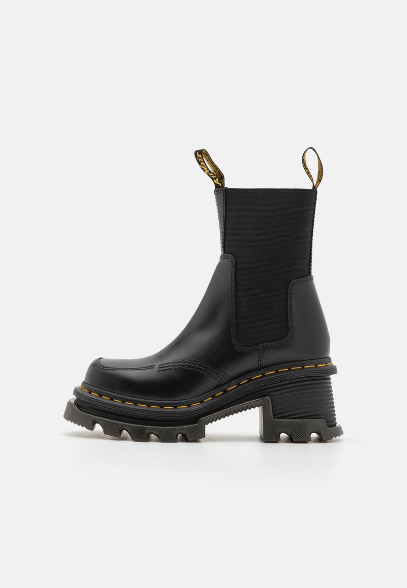Botte Chelsea en cuir noir avec semelle crantée épaisse, coutures jaunes, panneaux latéraux élastiques, boucles de talon et talon bloc.