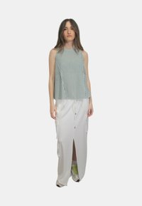 Top senza maniche a righe verde e bianco abbinato a una gonna bianca con spacco laterale e tasche laterali, caratterizzata da un dettaglio con coulisse.