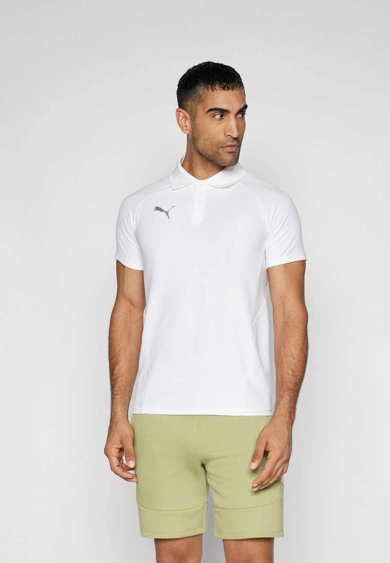 Weißes Poloshirt mit kurzen Ärmeln, Kragen und grauem Logo. Glatte Textur. Kombiniert mit hellgrünen Shorts mit seitlichen Taschen.