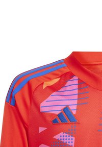 Maillot de sport rouge à manches courtes, avec des rayures bleues sur les épaules et des motifs géométriques en violet et orange. Logo Adidas en bleu.