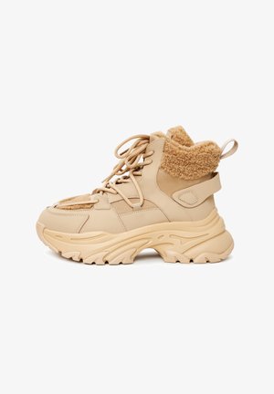 Beżowe sneakersy typu high-top z teksturowaną cholewką, futrzanym kołnierzem, sznurowanym przodem oraz masywną podeszwą z falistymi wzorami.