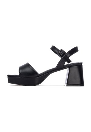 Sandalias de plataforma de cuero negro con puntera abierta redondeada, correa ajustable en el tobillo y un tacón grueso tipo bloque con un detalle metálico.