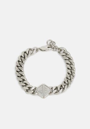 Bracelet en chaîne en métal argenté brillant avec des maillons épais, présentant un fermoir hexagonal avec des détails gravés.