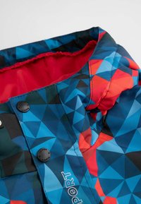 Kolorowa zimowa kurtka z geometrycznym wzorem w odcieniach niebieskiego, czerwonego i czarnego. Posiada gładką powierzchnię, podszewkę wewnętrzną oraz zatrzaski.