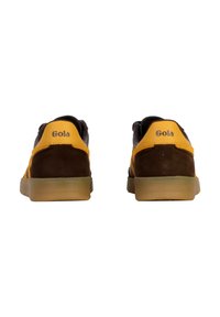 Un par de zapatillas Gola en marrón y amarillo vistas desde atrás, con suelas de goma y el nombre de la marca en las pestañas del talón.