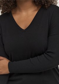 Haut noir à manches longues et col en V, fabriqué en tissu doux et côtelé ; manches ajustées avec accent texturé, corps ajusté pour plus de confort.