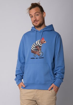 Blauwe sweatshirt met een berenafbeelding in een gestreept outfit op een eenwieler, met een rode beanie. Bevat een voorzak en een capuchon met koord.