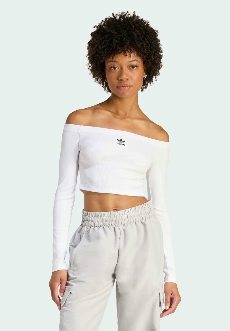 Biela crop top s odhalenými ramenami vyrobená z rebrovaného materiálu, s dlhými rukávmi a malým čiernym logom Adidas v strede.