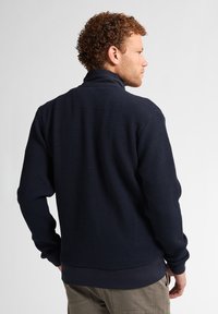 Granatowy sweter z teksturowanym wzorem plastra miodu. Posiada wysoki kołnierz oraz ściągacze na mankietach i u dołu dla lepszego dopasowania.