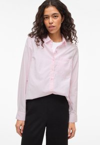 Jasnoróżowa koszula na guziki w pionowe paski, z pojedynczą kieszenią na piersi i długimi rękawami, w połączeniu z czarnymi spodniami.