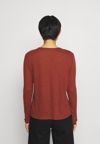 Långärmad skjorta i rödbrun färg, av lätt tyg. Åtsittande design med rundad halsringning och slät textur. Inga synliga mönster eller accenter.