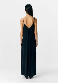 Abito maxi nero con scollatura a V bassa, spalline sottili e una silhouette fluida. Tessuto leggero con una leggera lucentezza e dettagli plissettati sul retro.