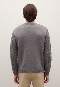 Maglione grigio lavorato a maglia con motivo a treccia testurizzato sulle maniche, collo e orlo a coste e corpo liscio. Vista posteriore semplice.