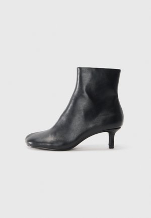 Stivale in pelle nera alla caviglia con punta affusolata e tacco sottile. Texture liscia e design senza cuciture, caratterizzato da un gambale alto e uno stile minimalista.
