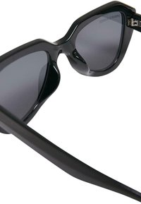 Ochelari de soare negri cu o formă îndrăzneață de cat-eye. Lentilele sunt întunecate, iar rama are o finisare lucioasă, având o balama singulară pe fiecare braț.