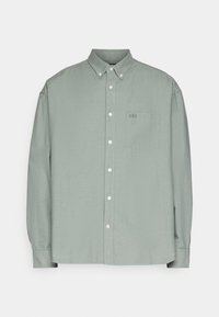 Chemise à manches longues vert clair en tissu lisse. Comprend un col, une poche avant, et un logo GAP discret sur la poche.