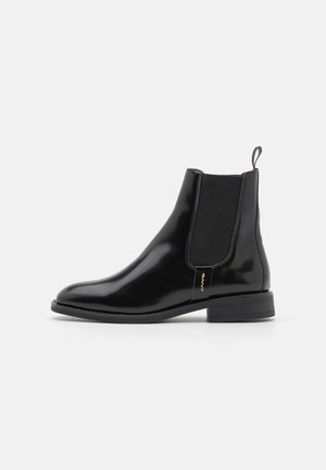 Botín Chelsea de cuero negro con paneles laterales elásticos, punta redonda y tacón bajo. Acabado brillante, cuenta con una lengüeta y un sutil detalle de marca.