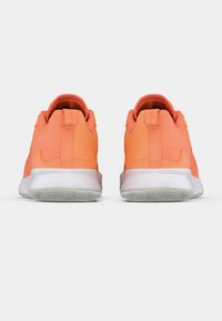 Ζευγάρι φωτεινά πορτοκαλί αθλητικά παπούτσια, ορατά από πίσω, με λευκές σόλες και λουράκια έλξης σε απλό λευκό φόντο.