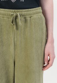Groene corduroy broek met verticale strepen, elastische tailleband en verstelbaar trekkoord. Zachte textuur en losse pasvorm.