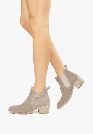 Bottines en suède gris avec un talon bloc, fermeture éclair sur le côté, panneaux élastiques et accents perforés. Texture lisse et design à bout arrondi.