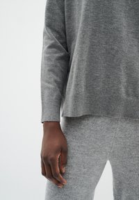 Gray knit sweater with a ribbed hem and cuffs, worn with matching gray knitted pants. Soft texture and relaxed fit are visible.