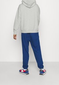 Felpa grigia, pantaloni jogger blu e sneakers con dettagli rossi. L'outfit presenta una silhouette rilassata, con polsini elastici e tasche laterali.