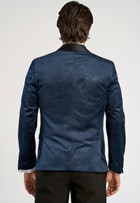 Mörkblå kavaj med paisleymönster, satinutseende och svart satinkrage. Har knäppte manschetter och en strukturerad siluett.