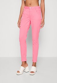 Pantalon en coton rose à coupe slim, avec poches avant, passants pour ceinture et fermeture éclair, assorti à des sandales blanches à talons blocs.
