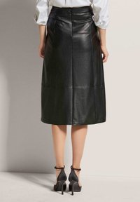 Schwarzer Echtleder-Midi-Rock mit glatter Textur, geradem Schnitt und sichtbaren Nahtdetails. Kombinierbar mit schwarzen High Heels.