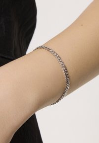 Srebrna bransoletka z metalowym wykończeniem, charakteryzująca się skręconym kształtem łańcuszka, gładką powierzchnią i lekko odbijającą światło, noszona na nadgarstku.