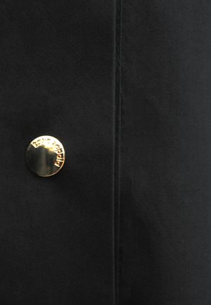 Czarna tkanina z pionowym szwem i pojedynczym błyszczącym złotym guzikiem z wygrawerowaną nazwą marki "Isabel Marant".