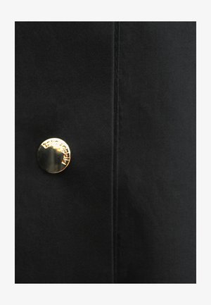 Czarna tkanina z pionowym szwem i pojedynczym błyszczącym złotym guzikiem z wygrawerowaną nazwą marki "Isabel Marant".