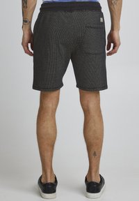 Shorts noirs texturés avec une coupe décontractée, dotés d'une poche arrière et d'une ceinture contrastante. Tissu lisse avec des détails de motif subtils.