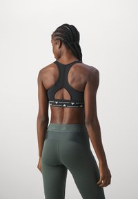 Zwarte sportbeha met een racerback ontwerp, featuring een sleutelgat uitsparing en een elastische band met merklogo. Gecombineerd met groene high-waisted leggings.