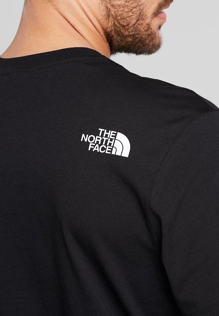 Mann trägt ein schwarzes T-Shirt mit dem weißen The North Face-Logo, das oben am Rücken nahe der Schulter gedruckt ist.